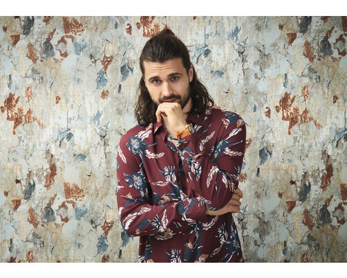 Mann mit floralem Hemd vor einer beschädigten Wand