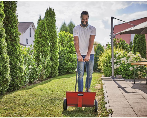Mann benutzt einen Düngerstreuer im Garten.