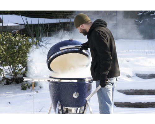Mann öffnet blauen Keramikgrill im verschneiten Garten