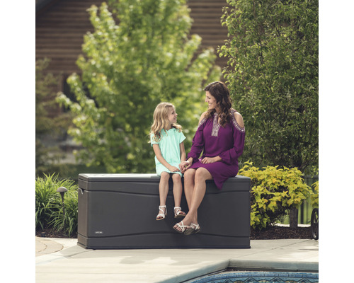 Mutter und Tochter sitzen auf einer grauen Gartenbox aus Kunststoff im Garten.