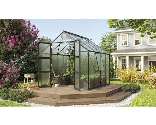 Gewächshaus Vitavia Olymp 6700 Hohlkammerplatten 4 mm 257 x 261 cm smaragd Gewächshaus mit geöffneten Türen und Pflanzen auf einer Holzterrasse in einem Garten.