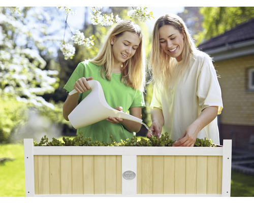 Deux femmes arrosent des plantes dans un potager surélevé avec un arrosoir dans le jardin.