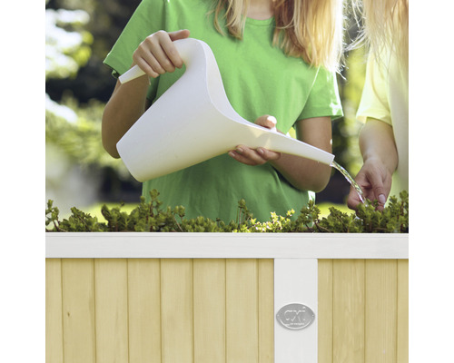Enfant arrosant des plantes avec un arrosoir dans une jardinière surélevée.
