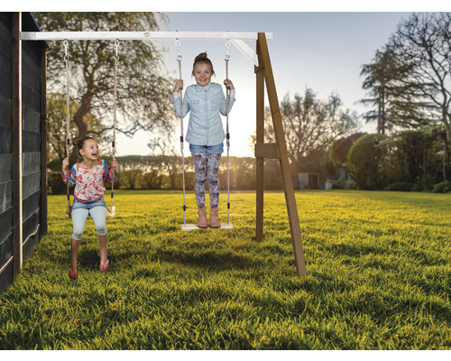 Deux enfants se balancent sur une balançoire en bois dans le jardin.