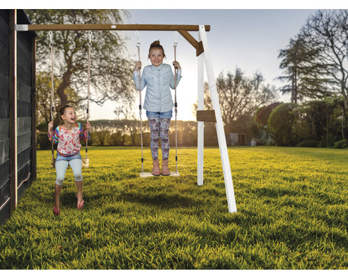 Deux enfants se balancent sur une balançoire en bois dans le jardin.