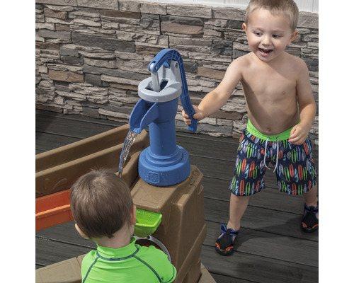 Des enfants jouent avec une pompe à eau sur une table à sable et à eau