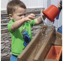 Bambin versant de l''eau d''un seau dans une table de jeu