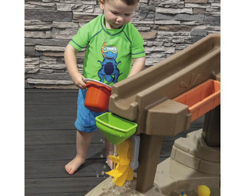 Un jeune enfant joue avec une table de jeu d''eau avec toboggan, entonnoir et seau dans le jardin