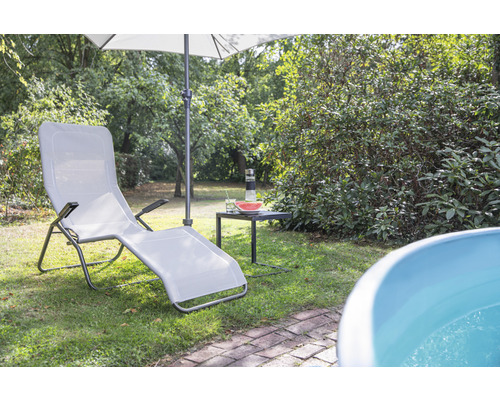 Scène de jardin avec une chaise longue, un parasol et une petite table