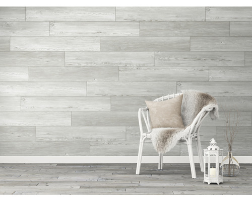 Wandpaneele in Holzoptik, weisser Stuhl mit Kissen und Decke, Laterne und Vase mit Zweigen in einem hellen Raum.