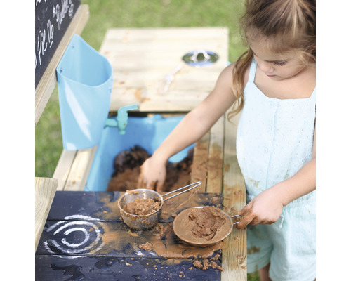 Fille jouant avec une cuisine boueuse dans le jardin