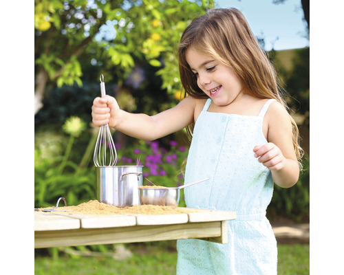 Fille jouant avec des casseroles, du sable et un fouet dans le jardin