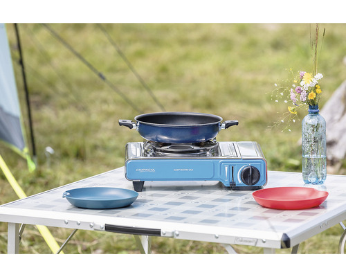 Campingtisch mit Gaskocher, Bratpfanne und Geschirr im Freien