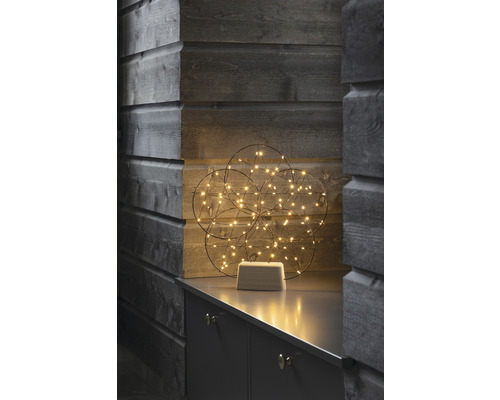 Dekorative Leuchtkugel mit LED-Lichtern auf einem grauen Möbelstück vor einer Holzwand.