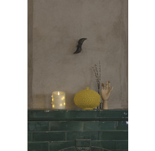 Scène décorative avec bougie LED, vase à pointes et main en bois sur une corniche de carreaux verts.