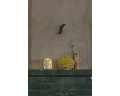 Scène décorative avec bougie LED, vase à pointes et main en bois sur une corniche de carreaux verts.
