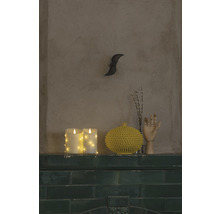 Scène décorative avec des bougies LED, un vase jaune, un modèle de main en bois et une décoration murale sur une étagère.
