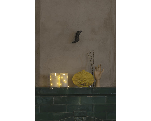 Scène décorative avec des bougies LED, un vase jaune, un modèle de main en bois et une décoration murale sur une étagère.
