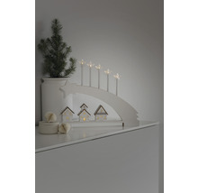 Dekorative Weihnachtsszene mit Lichterbogen, Sternkerzen, kleinen Häusern und einer Topfpflanze.