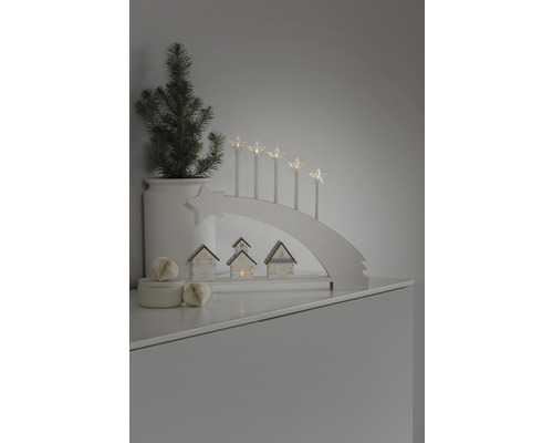 Dekorative Weihnachtsszene mit Lichterbogen, Sternkerzen, kleinen Häusern und einer Topfpflanze.