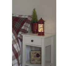 Table de chevet avec décorations de Noël, comprenant une boule à neige avec un motif de Père Noël et une plante en pot