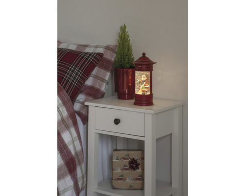 Table de chevet avec décorations de Noël, comprenant une boule à neige avec un motif de Père Noël et une plante en pot