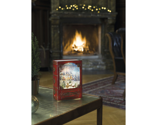 Boule à neige décorative en forme de livre avec motif de Noël devant la cheminée