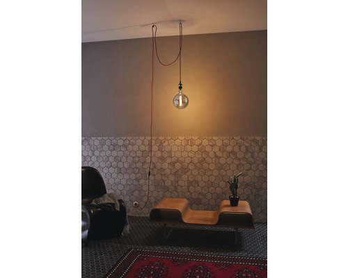 Photo d'intérieur d'un salon avec une seule ampoule comme suspension, un fauteuil, une table en bois et un tapis rouge.