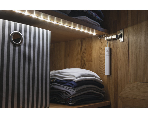 Innenansicht eines Schranks mit LED-Beleuchtung, einem gestreiften Aufbewahrungskorb und gefalteter Kleidung.