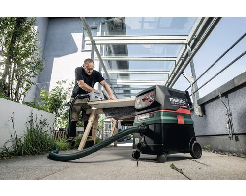 Artisan coupant du bois avec une scie circulaire à main et un aspirateur industriel