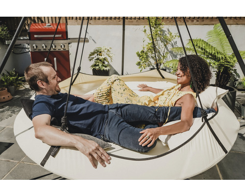 Ein Paar entspannt in einem runden Hängesessel im Garten.