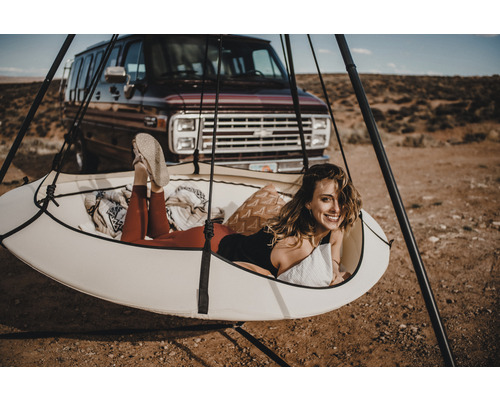 Frau entspannt in einem Hängezelt mit Stativ im Freien vor einem Lieferwagen.