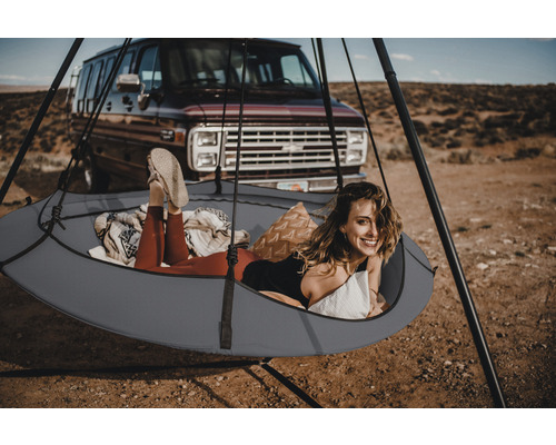 Frau entspannt in einer Hängehöhle mit Gestell vor einem Auto in der Natur