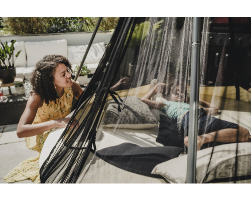 Szene im Garten mit Mutter und Kind unter einem Pavillon mit Moskitonetz auf einem Tagesbett mit Kissen.