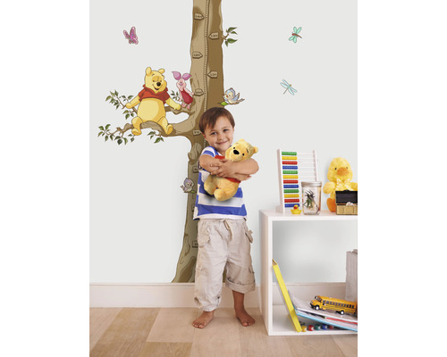 Garçon étreignant une peluche devant un tableau de croissance autocollant mural Winnie l''ourson dans une chambre d''enfant