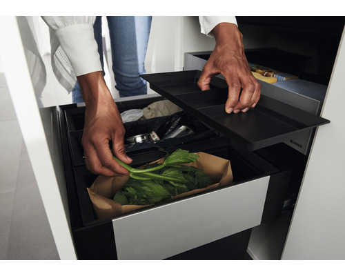 Une personne jette des déchets végétaux dans une poubelle coulissante Blanco