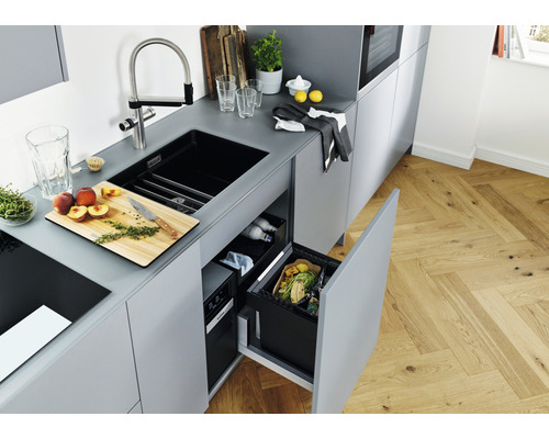 Cuisine moderne avec évier, robinet, planche à découper avec pêches et système de poubelle coulissante ouvert