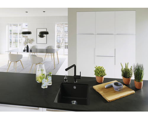 Helle Küche mit schwarzer Spüle, Armatur, Kräutern im Topf, Schneidebrett und Esstisch