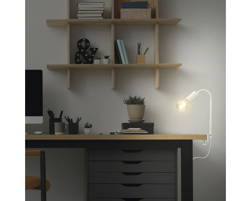 Espace de travail avec bureau, étagères et une lampe à pince blanche.
