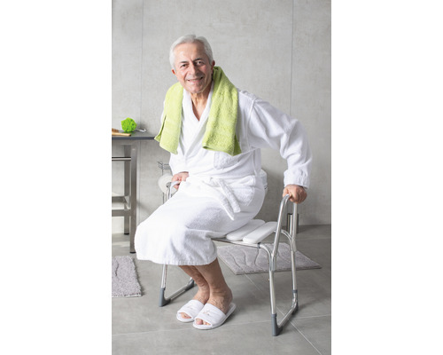 Un homme est assis sur un tabouret de douche avec accoudoirs dans la salle de bain.