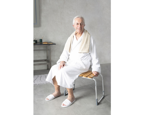 Un homme est assis sur un banc de douche avec des lattes en bois et un cadre en aluminium dans la salle de bain