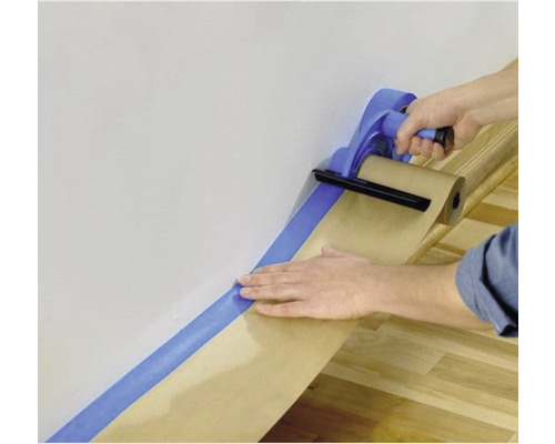 Person bringt Malerkrepp mit Abdeckpapier an der Wand an.