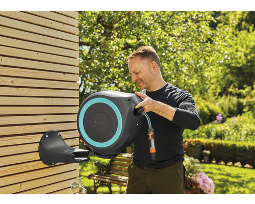 Un homme utilise un dévidoir mural dans le jardin.