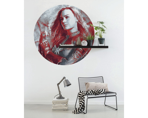 Wanddekoration mit Captain Marvel Motiv über einem Regal mit Dekorationsgegenständen, Lampe und Stuhl im Raum.