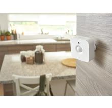 Détecteur de mouvement Philips Hue blanc monté sur une surface en bois clair dans une cuisine lumineuse et organisée.