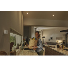 Détecteur de mouvement blanc sur un mur dans une cuisine moderne avec une femme portant un sac de courses.