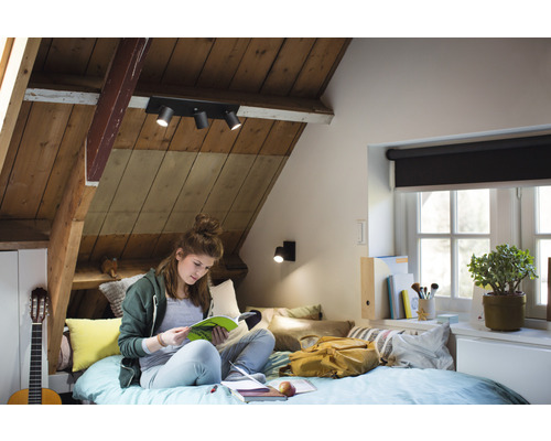 Chambre mansardée lumineuse avec spots de plafond et personne en train de lire