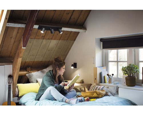 Chambre mansardée lumineuse avec plafond en bois, éclairée par un plafonnier à trois spots et une applique murale.