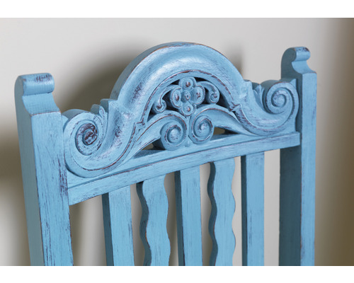 Detailansicht der Rückenlehne eines hellblauen Holzstuhls mit dekorativen Schnitzereien