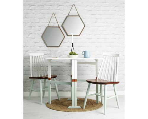 Salle à manger avec table, chaises et deux miroirs hexagonaux sur un mur de briques